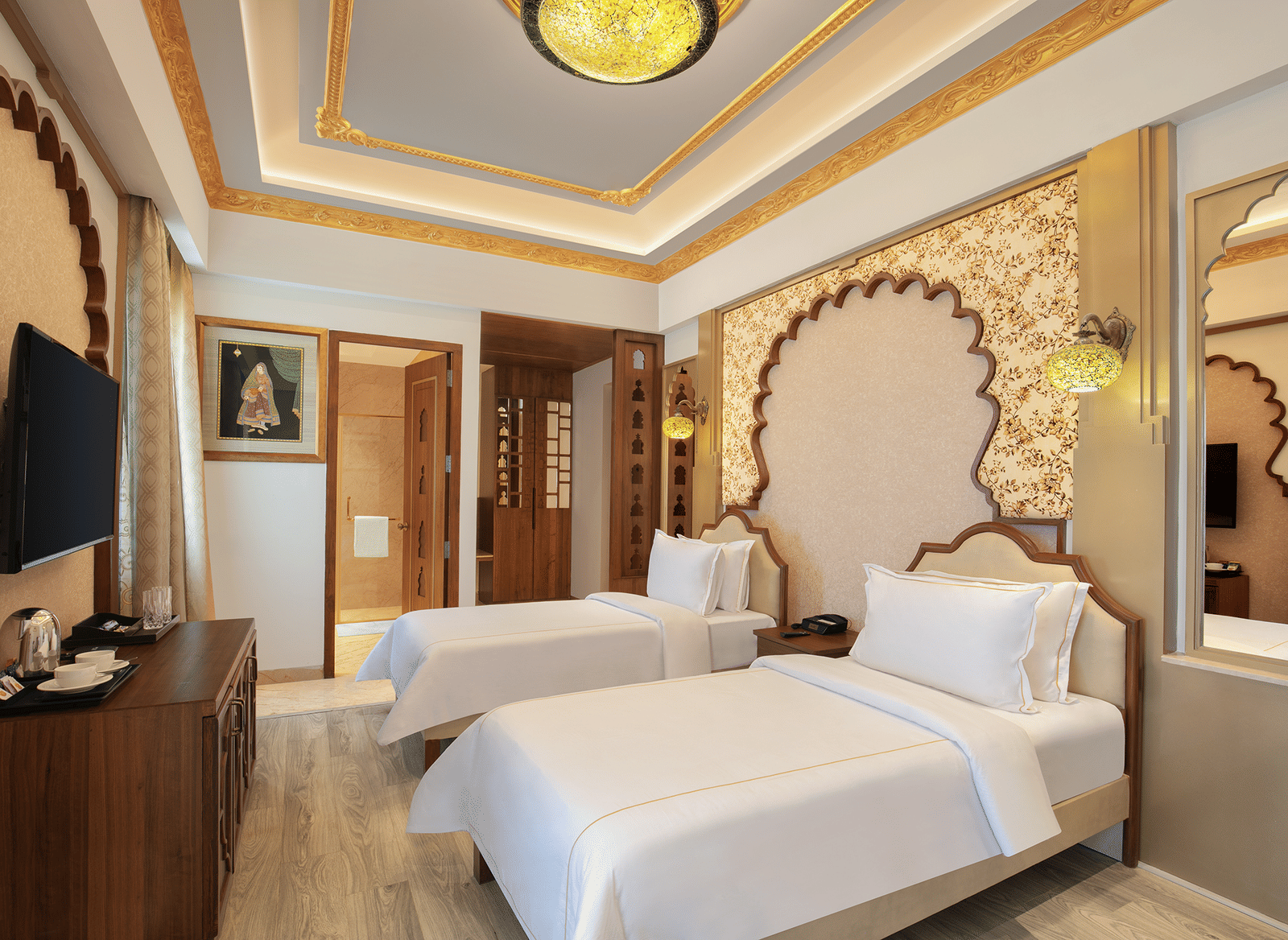 A room with twin beds, ornate golden accents, and a decorative wall panel – Kaldan Samudra, a luxurious beach resort in ECR