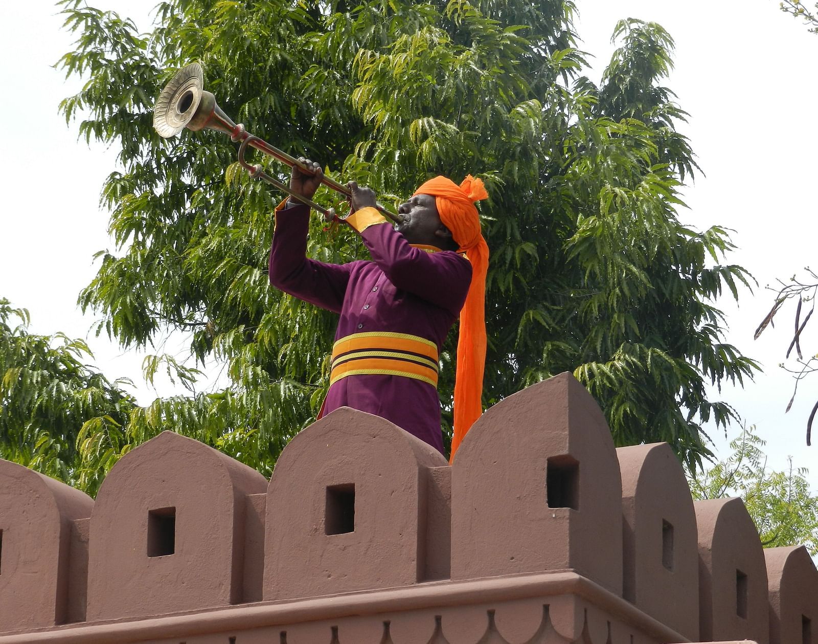 A man in traditional attire playing an instrument atop a fortified wall  - Khas Bagh, Jaipur.