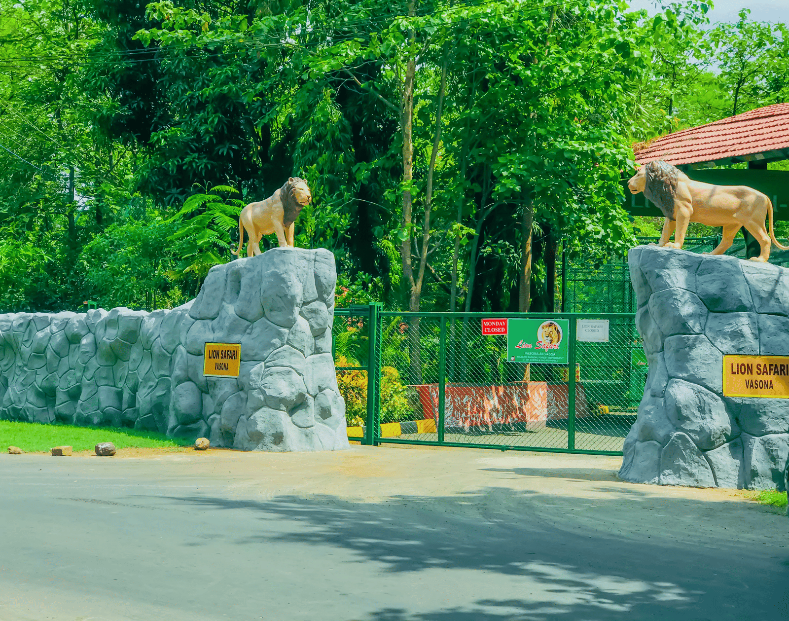 Entrance to a park or wildlife reserve featuring a green gate, stone wall with animal sculptures, and lush foliage.