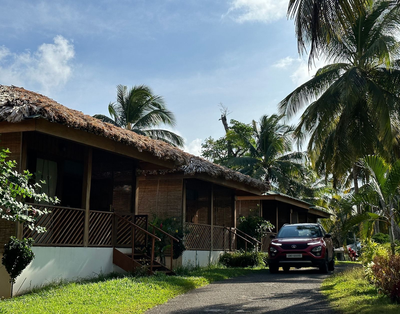 A charming resort building with a thatched roof, surrounded by lush green grass and palm trees under a bright sky.