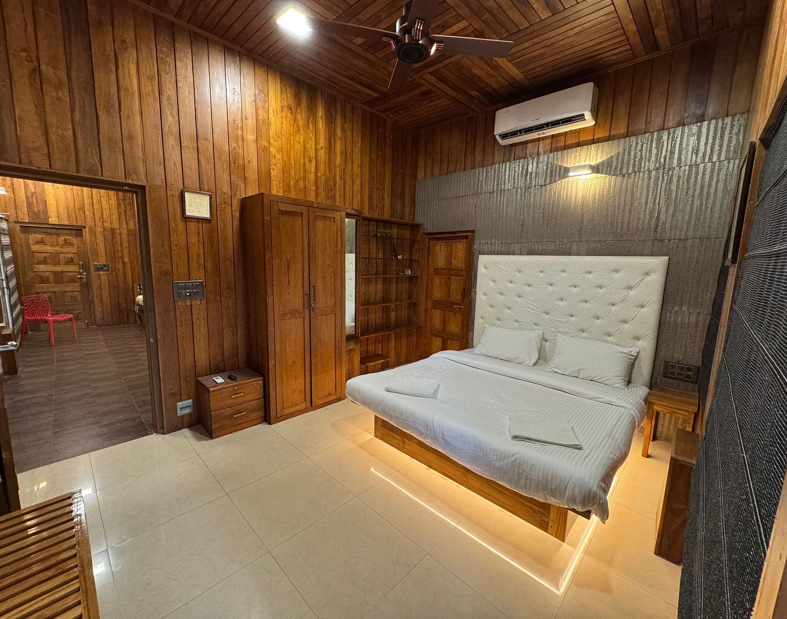A bedroom with rich wooden walls and ceiling, a platform bed with a white tufted headboard, and a ceiling fan.