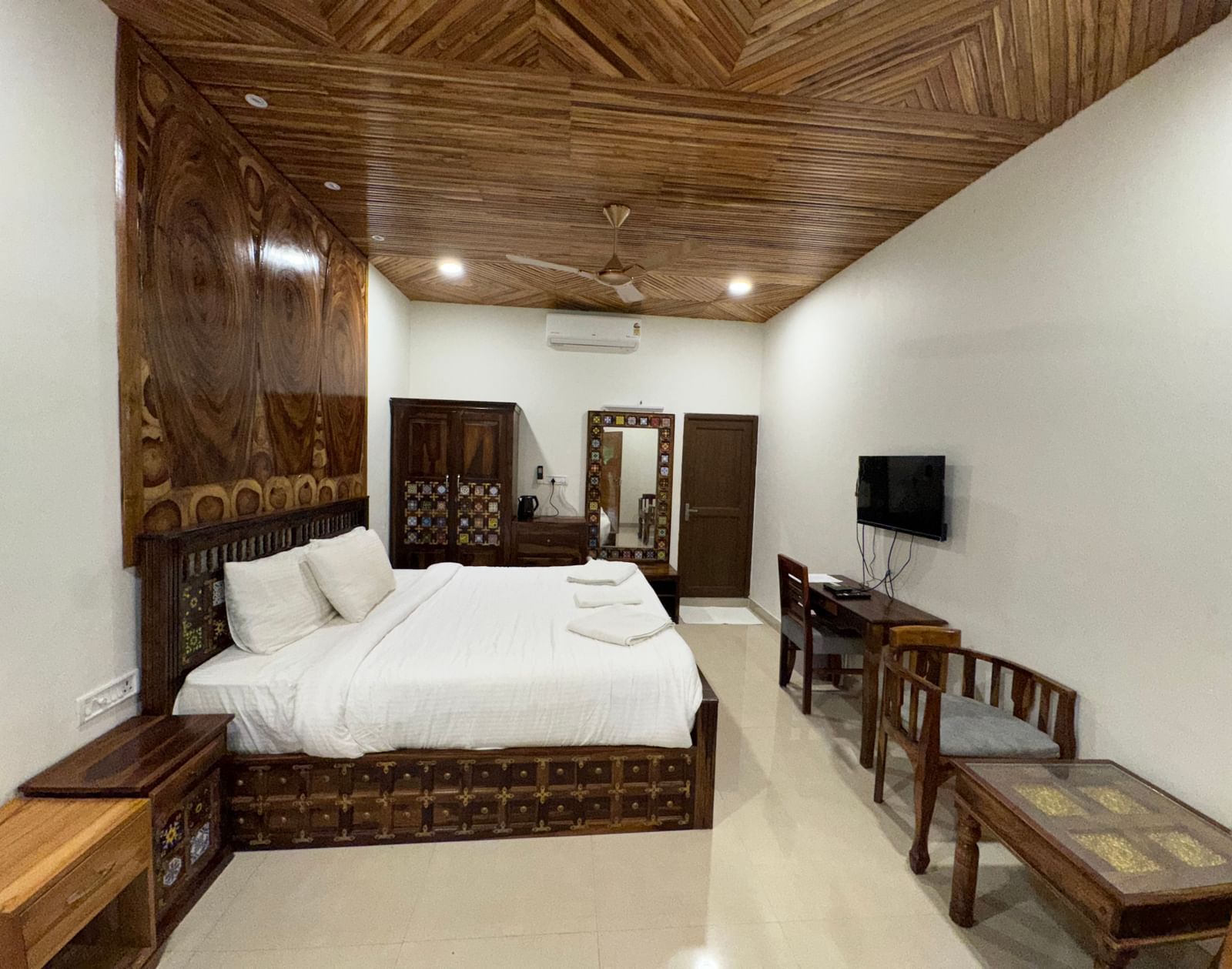 A bedroom with a large bed, wooden furniture, a TV, and a unique patterned wooden ceiling at RainForest Resort.