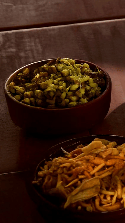 Close-up of an Indian meal featuring a brass bowl of spicy curry, small baked buns (pav), and side bowls of sprouted lentils and namkeen.