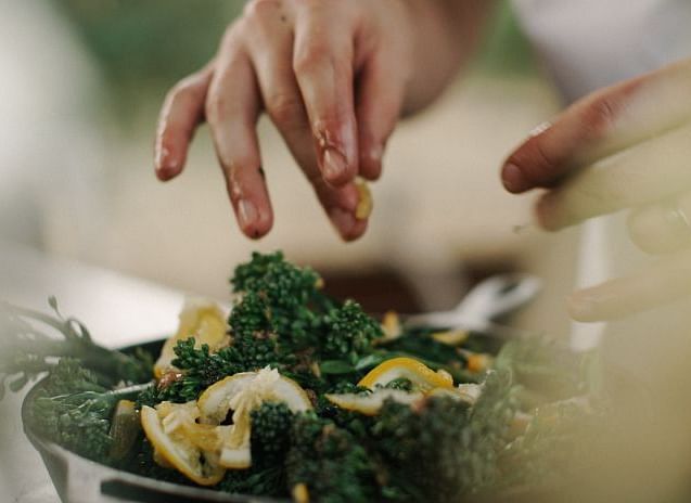 Hands seasoning a green leafy salad with slices of lemon in a blurred kitchen setting - BluSalzz Collection - Tranquil Resort, Wayanad