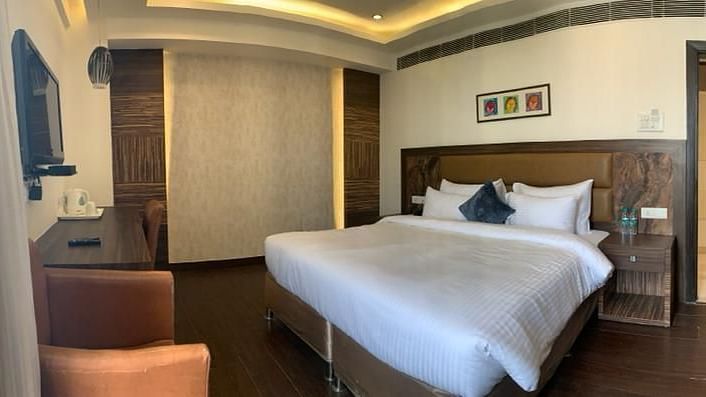 A close-up of a neatly made bed in a hotel room, with a partially visible sofa - VITS Gurugram
