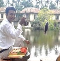 A person in traditional attire standing in a flooded area, holding an object and looking at the water