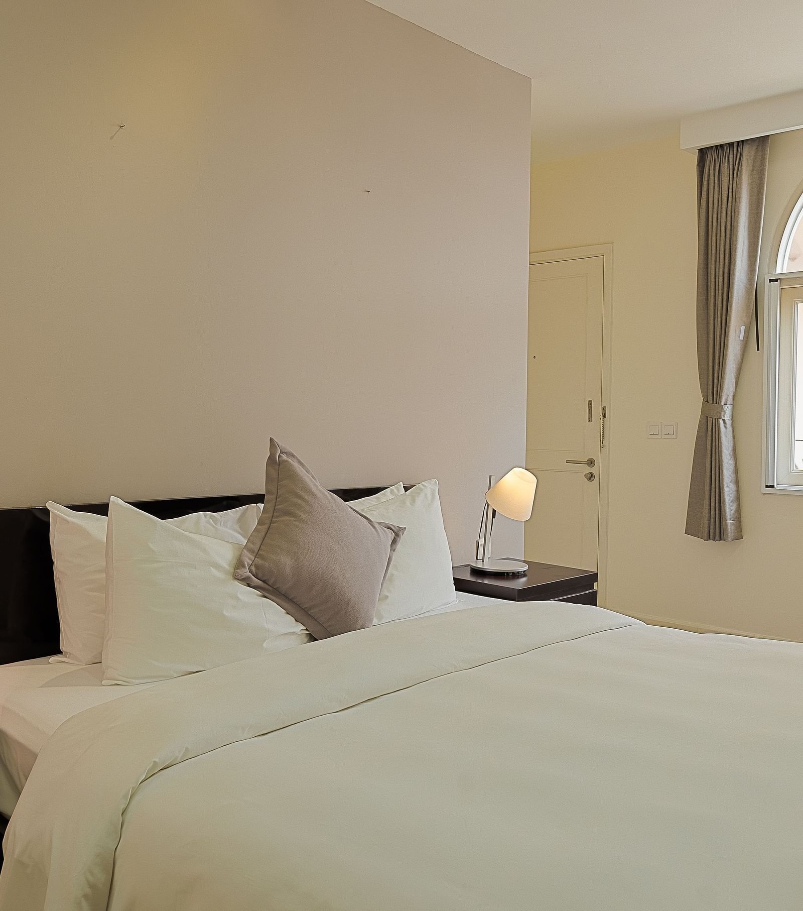 A room with a white bed, bedside tables, lamps, and a large window | Four-bedroom Suite | Central Mansions, Phnom Penh