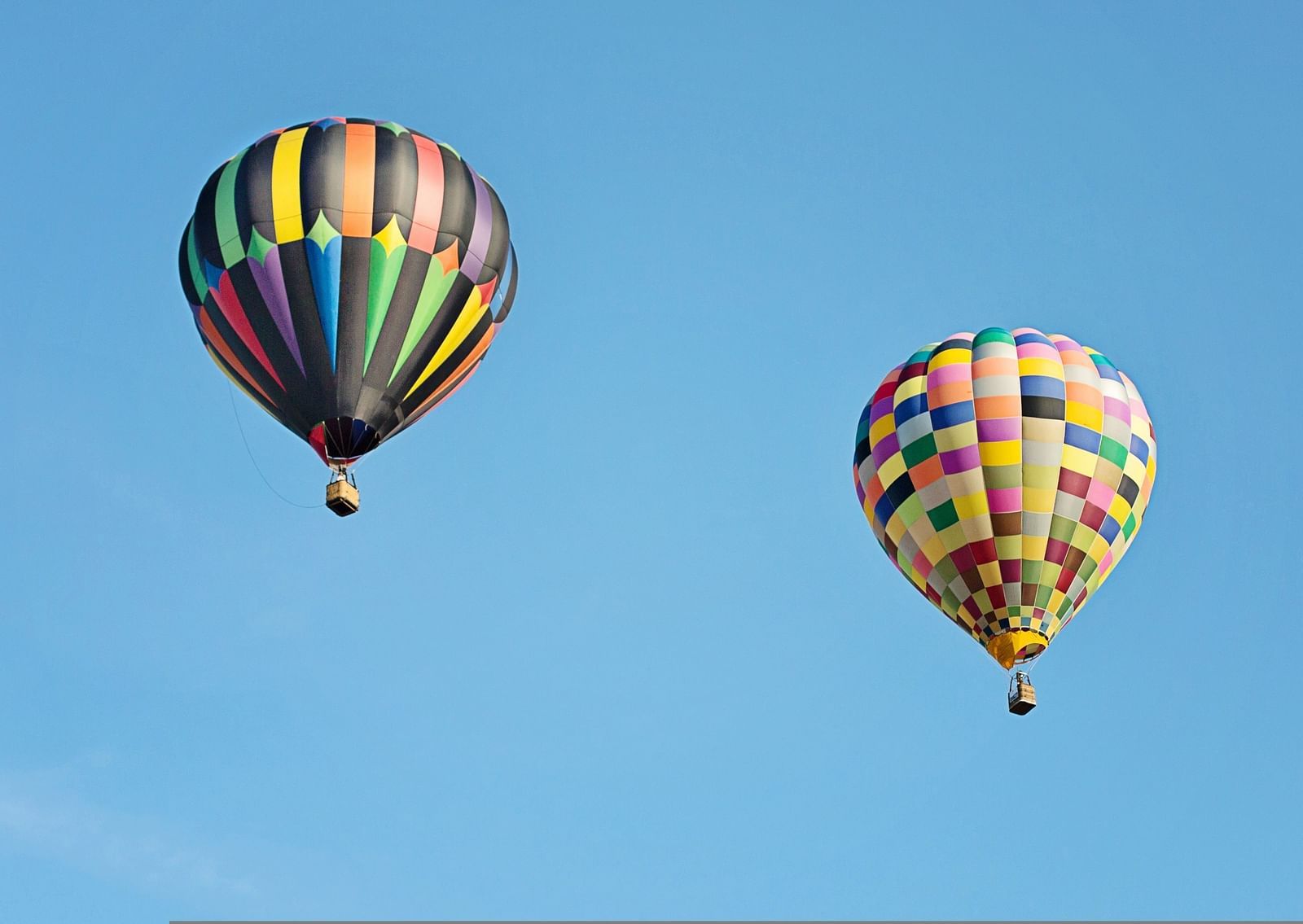 Two hot air balloons in the sky as seen from below with blue sky in the background.