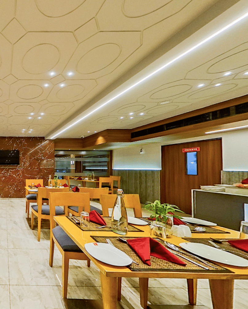 Contemporary restaurant with wooden dining tables, black chairs and red napkins at Lords Eco Inn Dahej, set for guest dining service