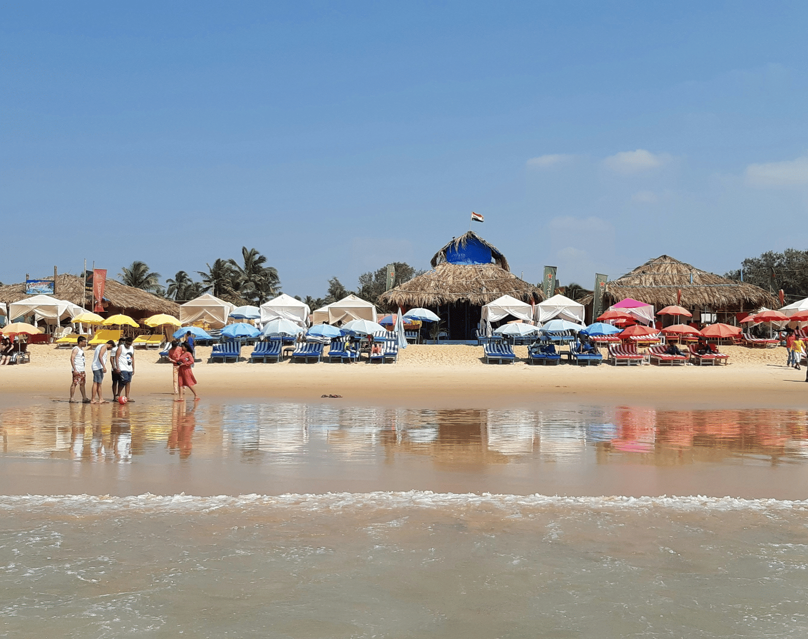A vibrant, wide beach is packed with colourful parasols and sunbeds, with a strip of small buildings lining the shore.