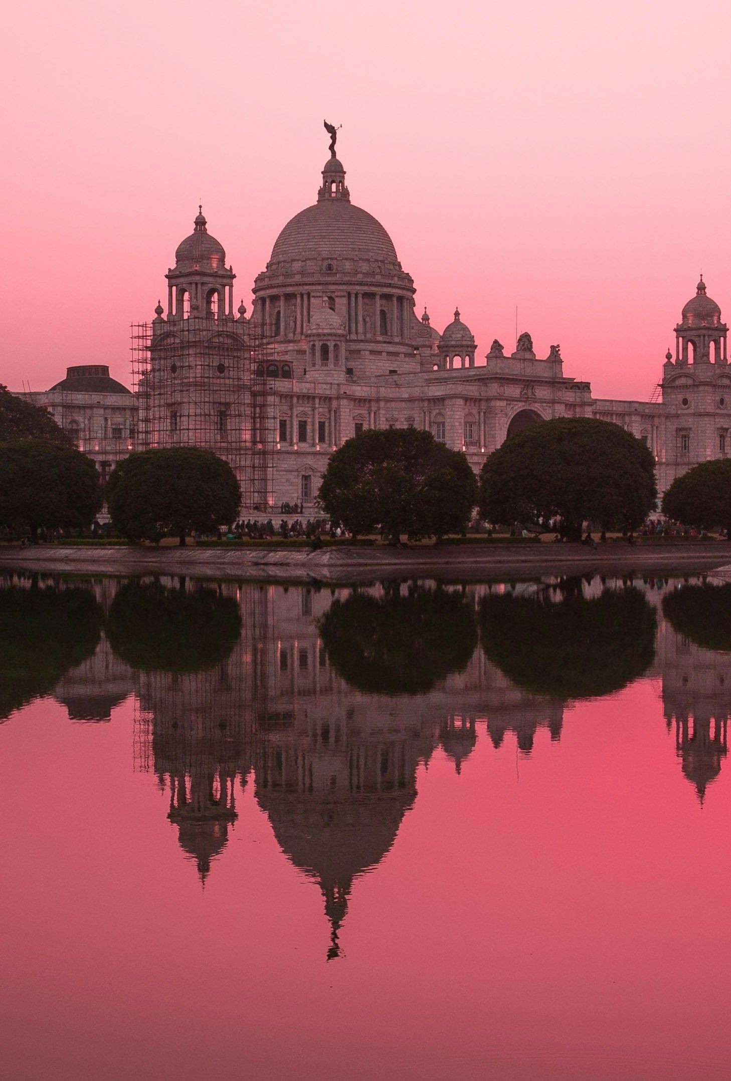 The stunning Victoria Memorial palace reflected perfectly in a calm lake at dawn.