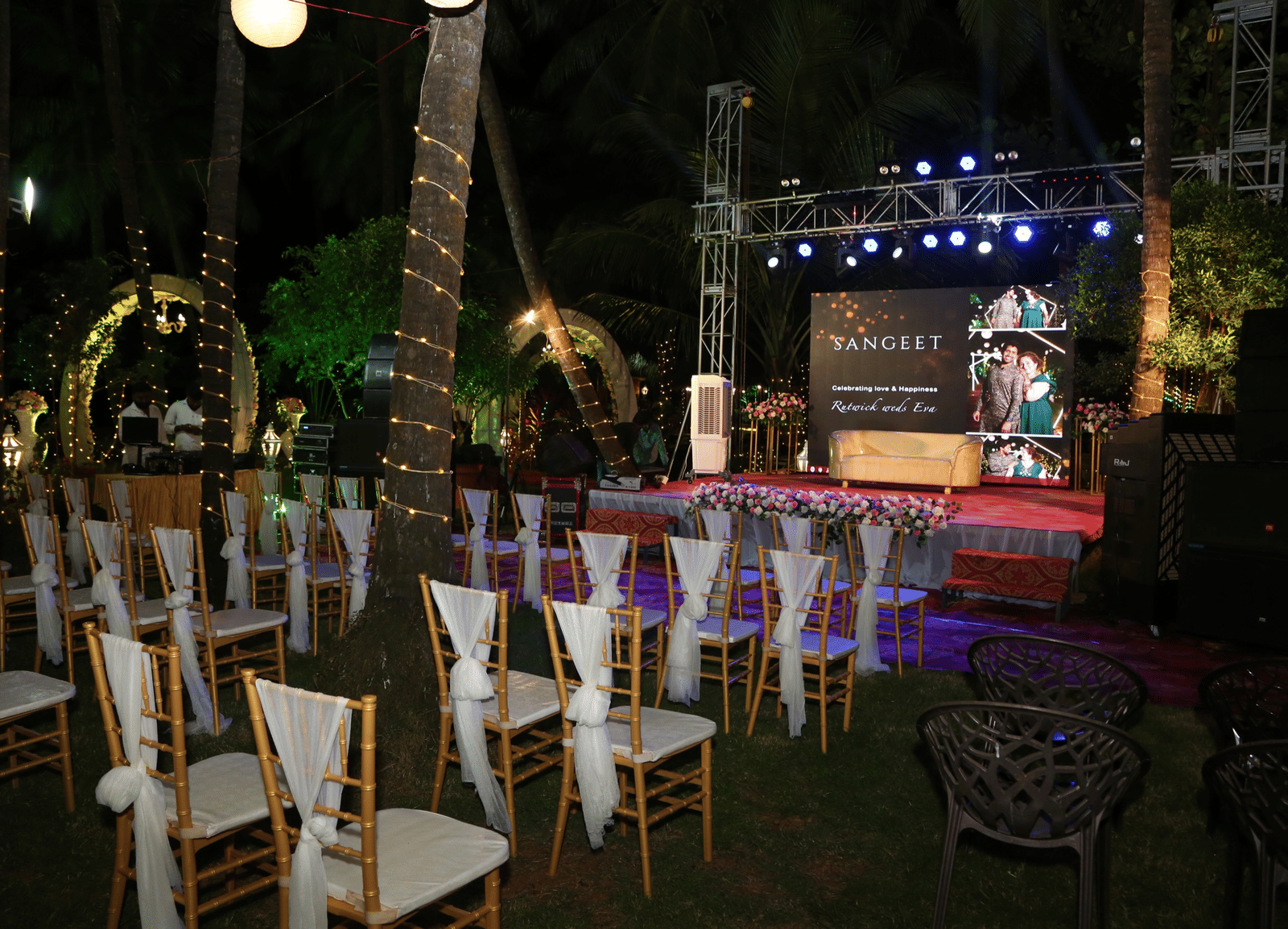 Outdoor seating with white chairs arranged before decorated stage at Paradise Lagoon Resort, Udupi.