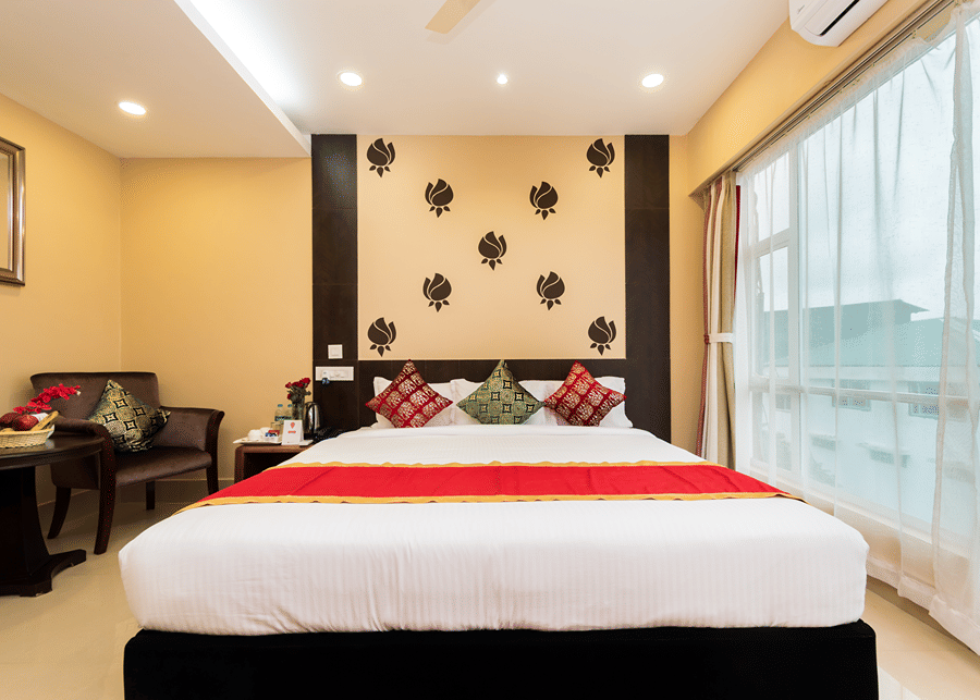 One of the Deluxe Rooms near sSliguri Junction at Central Courtyard Boutique Hotel featuring a double bed under bright lighting next to a large window against a patterned wall