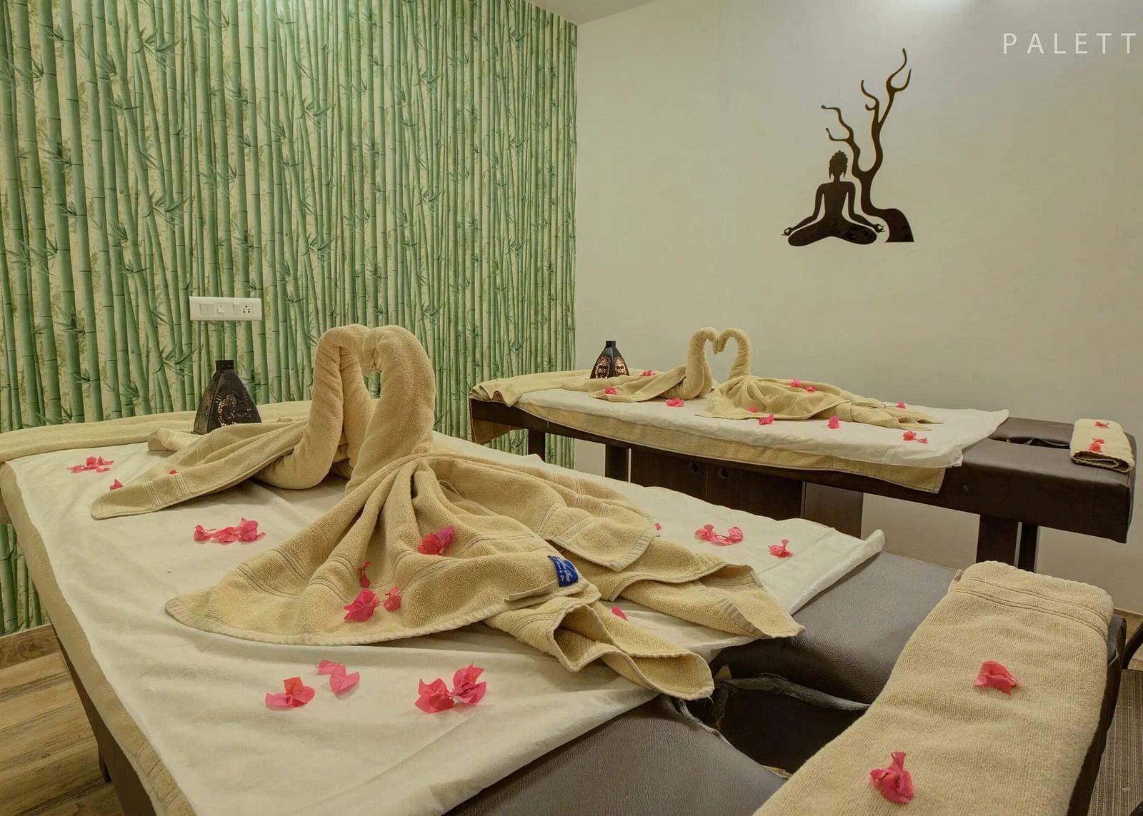 Cosy spa room with two massage tables, folded towels, rose petals, and a bamboo-themed wall. - Bamboo Saa, Udaipur
