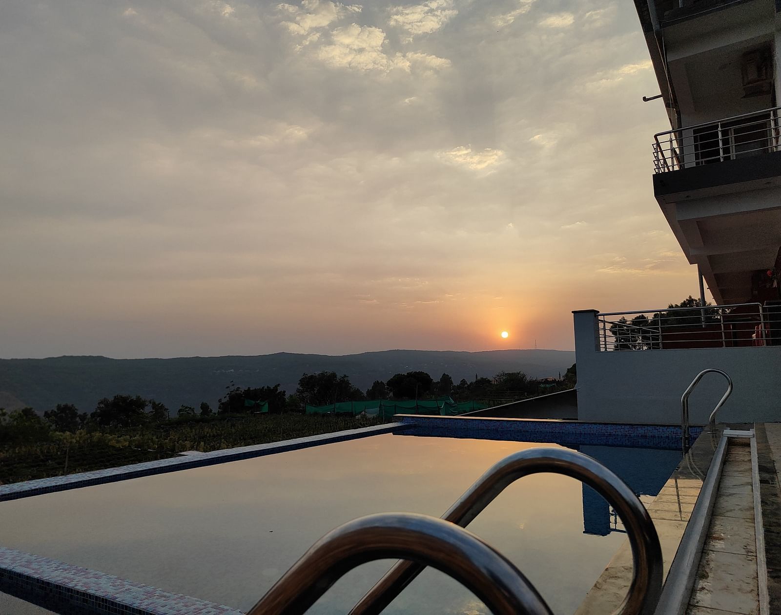 A view of the swimming pool overlooking the sunset surrounded by hills.