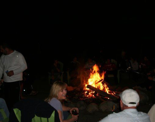 A campfire event at Kit Carson Lodge & Restaurant shows two people sitting near a fire at night. 