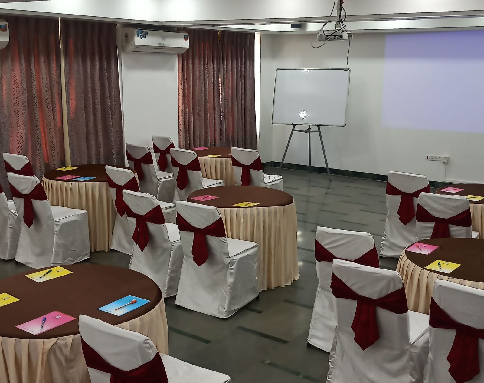Training room setup with cluster seating arrangement, notepads, and a projection screen at Mayur Retreat.