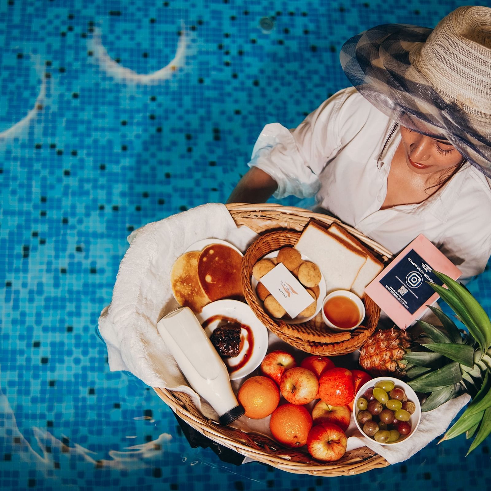 An overhead of a woman enjoying a dish with meat and vegetables in a swimming pool | Mansha Hotels