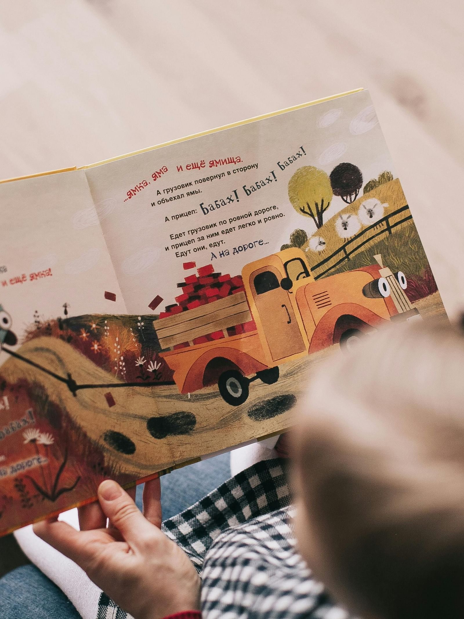 A person is seen from behind reading an open storybook with colourful illustrations.