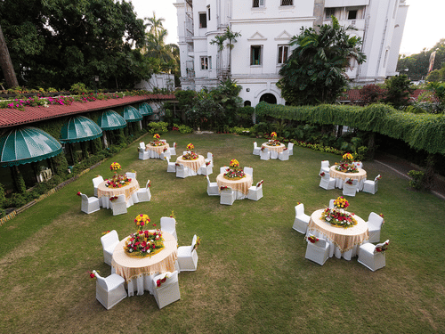 Round table seating arrangement on the lawn area at Kenilworth Hotel, Kolkata, with trees and buildings surrounding the lawn area. 