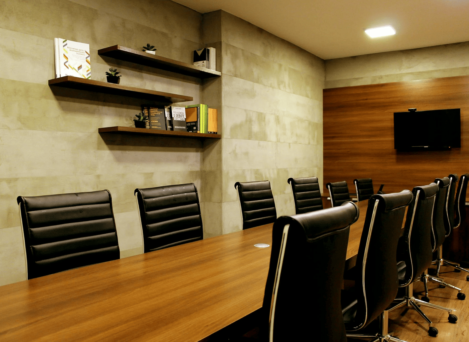 An image of a conference room with table, chairs and a tv mounted to the wall.