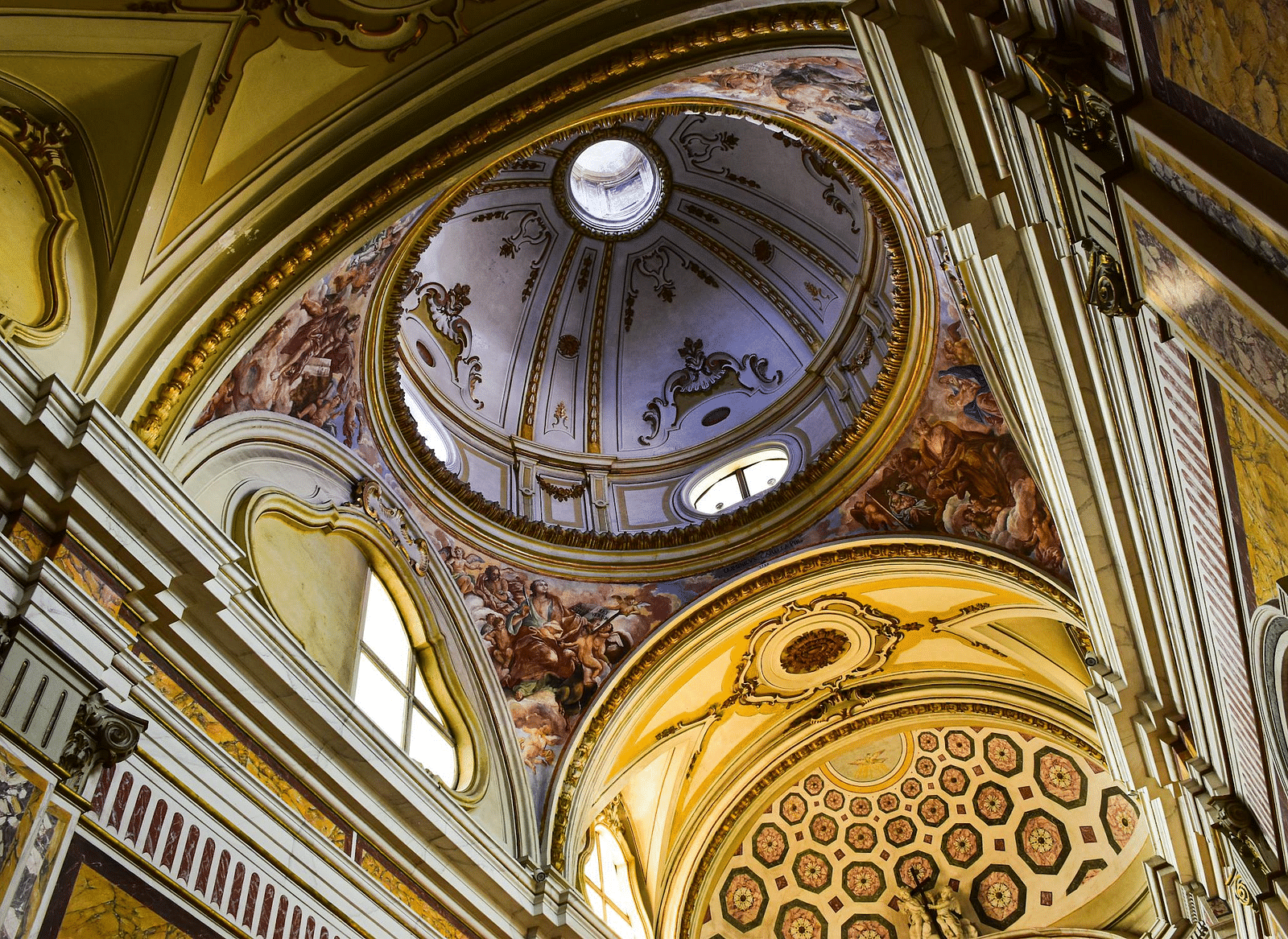 A beautifully decorated church ceiling with golden accents, elaborate frescoes, and a central dome.