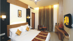 A Deluxe Room at Hotel Southern Regency, Karol Bagh, Delhi, with a bed, warm lighting, full length curtains, a wall-mounted TV, work desk, and seating area.