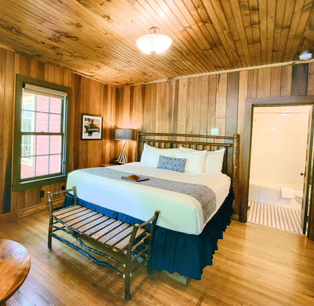 a wide angle shot of a bedroom with a modern looking table lamp kept on the round wooden coffee table - Historic Tapoco Lodge