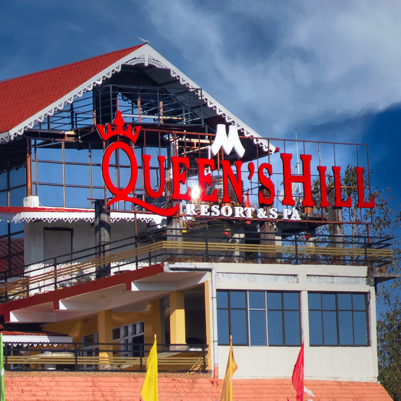 Mount Queens Hill Lake Resort & Spa in Mirik featuring a sloped red-roof structure with large glass windows, terrace seating, and vibrant hillside surroundings | A unit of Mount Hotels in North Bengal