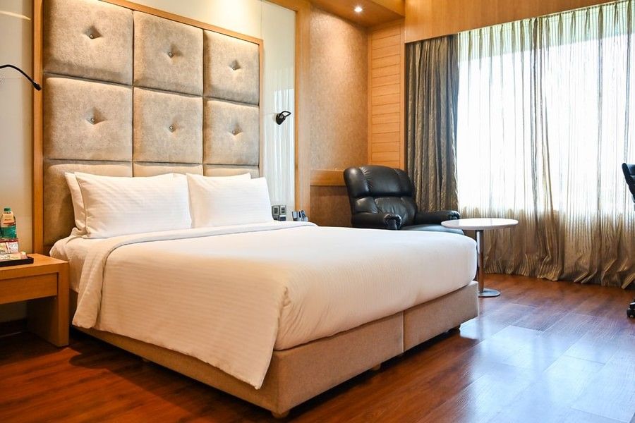 A well-appointed hotel room with a large bed, wooden headboard, and elegant furnishings, suggesting comfort and luxury.