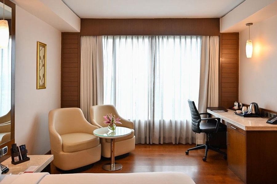 A spacious hotel suite featuring a seating area, desk, and large windows, offering a comfortable stay.