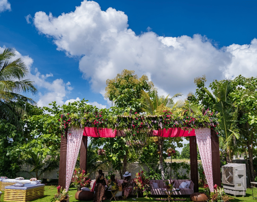 An outdoor wedding canopy or mandap decorated with pink and white fabrics and flowers, set on a green lawn under a bright blue sky - Grande Bay Resort & Spa, Mamallapuram