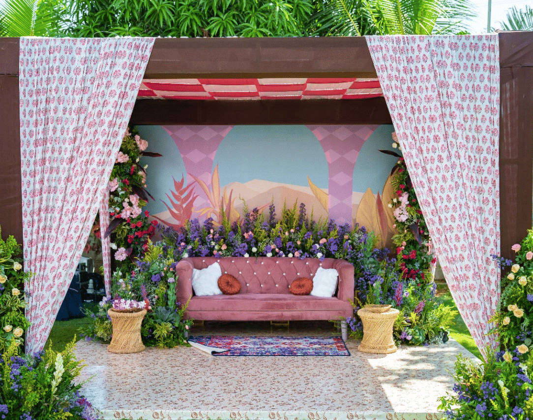 An outdoor wedding stage or mandap with a pink and white floral and fabric theme, featuring a seating area, set on a green lawn - Grande Bay Resort & Spa, Mamallapuram