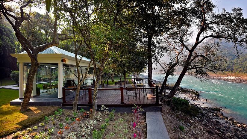 Patio alongside trees and emerald green river Ganga