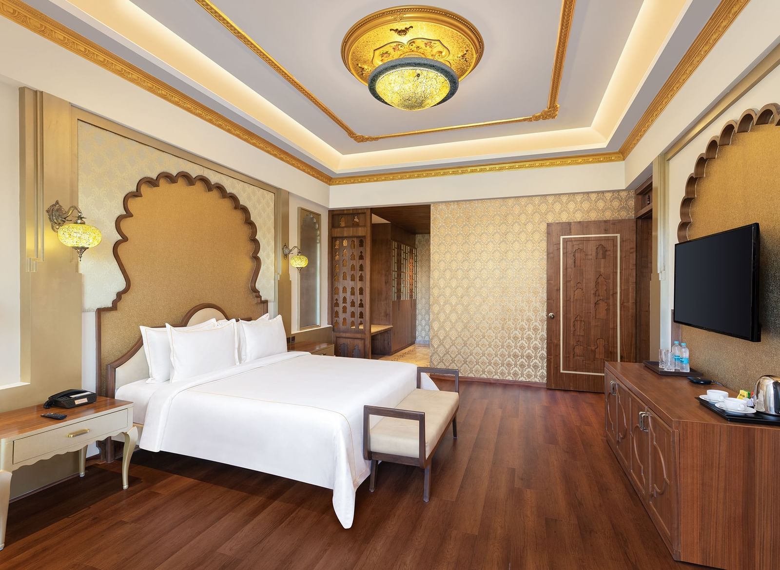 A sophisticated bedroom with wooden floors, golden accents, and plush white bedding – Kaldan Samudra, one of the finest luxury hotels in Mahabalipuram