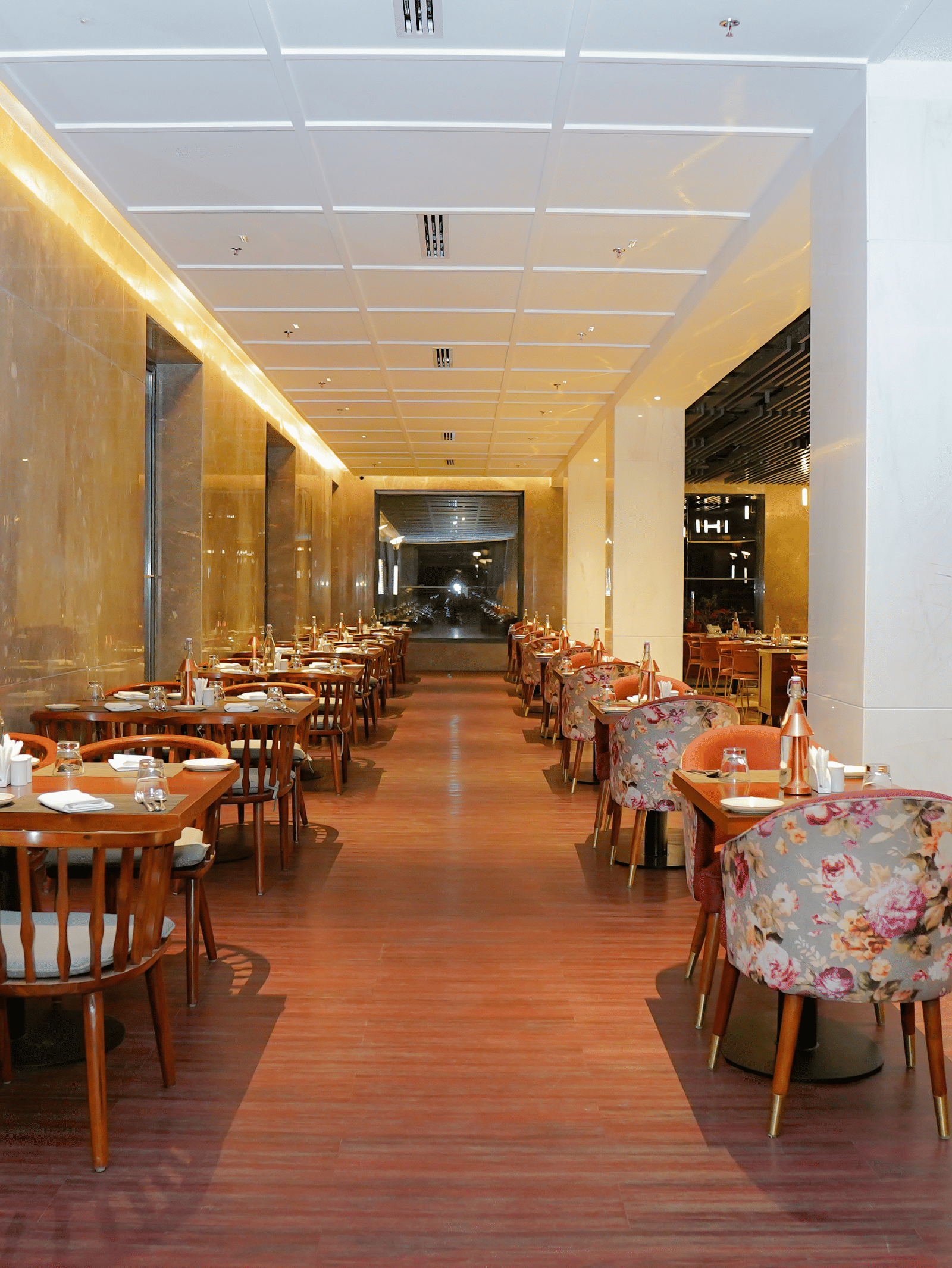 A long, well-lit indoor dining corridor with wooden and floral upholstered seating at Pushkara Resort & Spa.