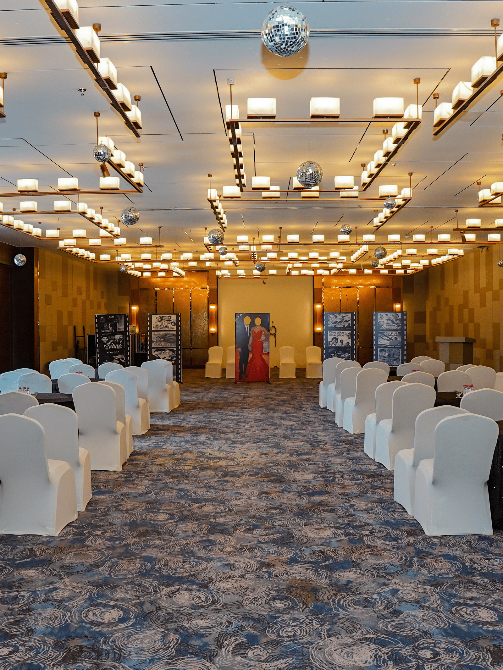 A view of a long event hall set up with multiple rows of chairs for an audience, showing the full length of the room.