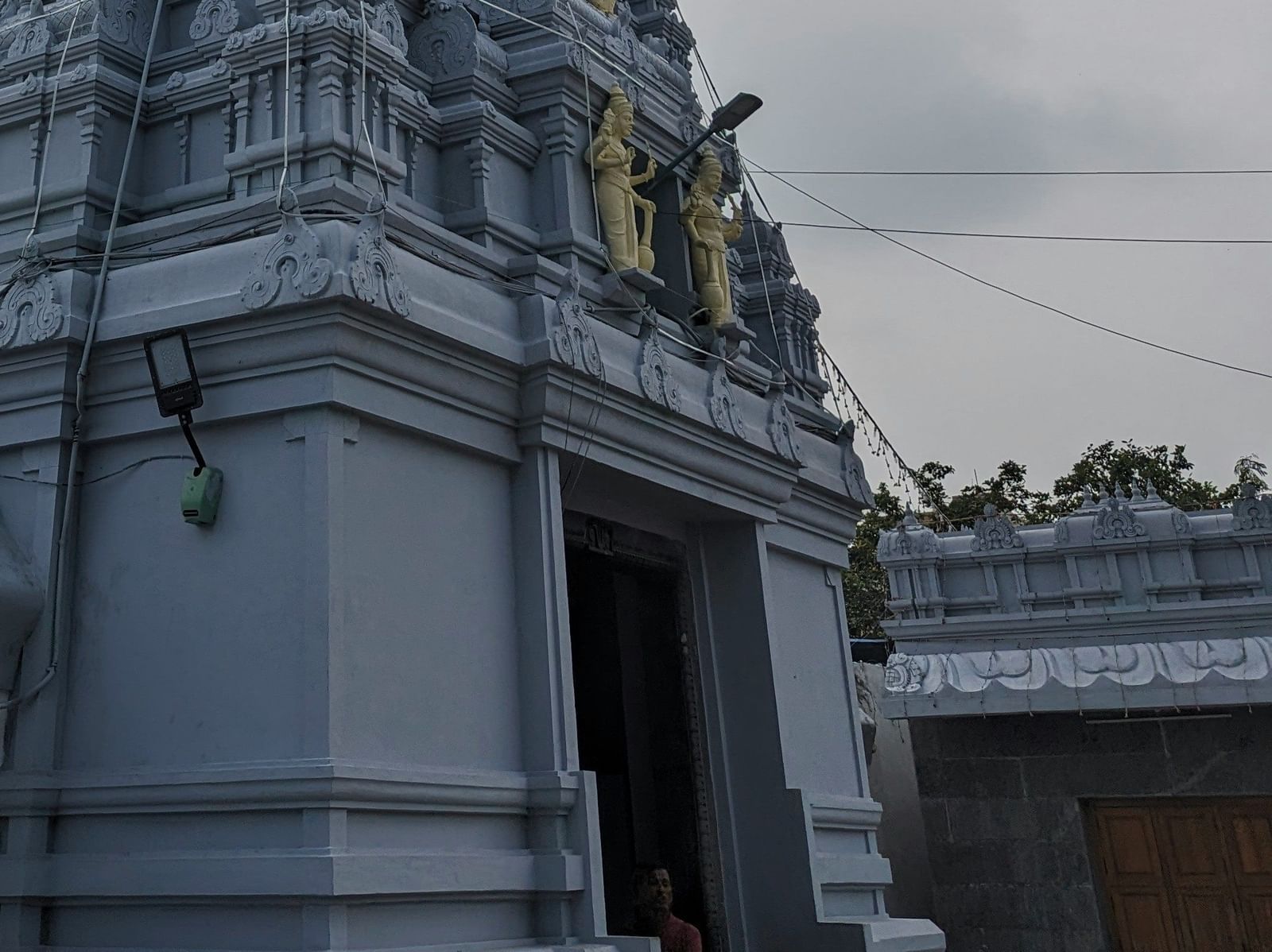 A tall, tiered tower of a white temple with a flagpole  visible to the right under a cloudy sky.