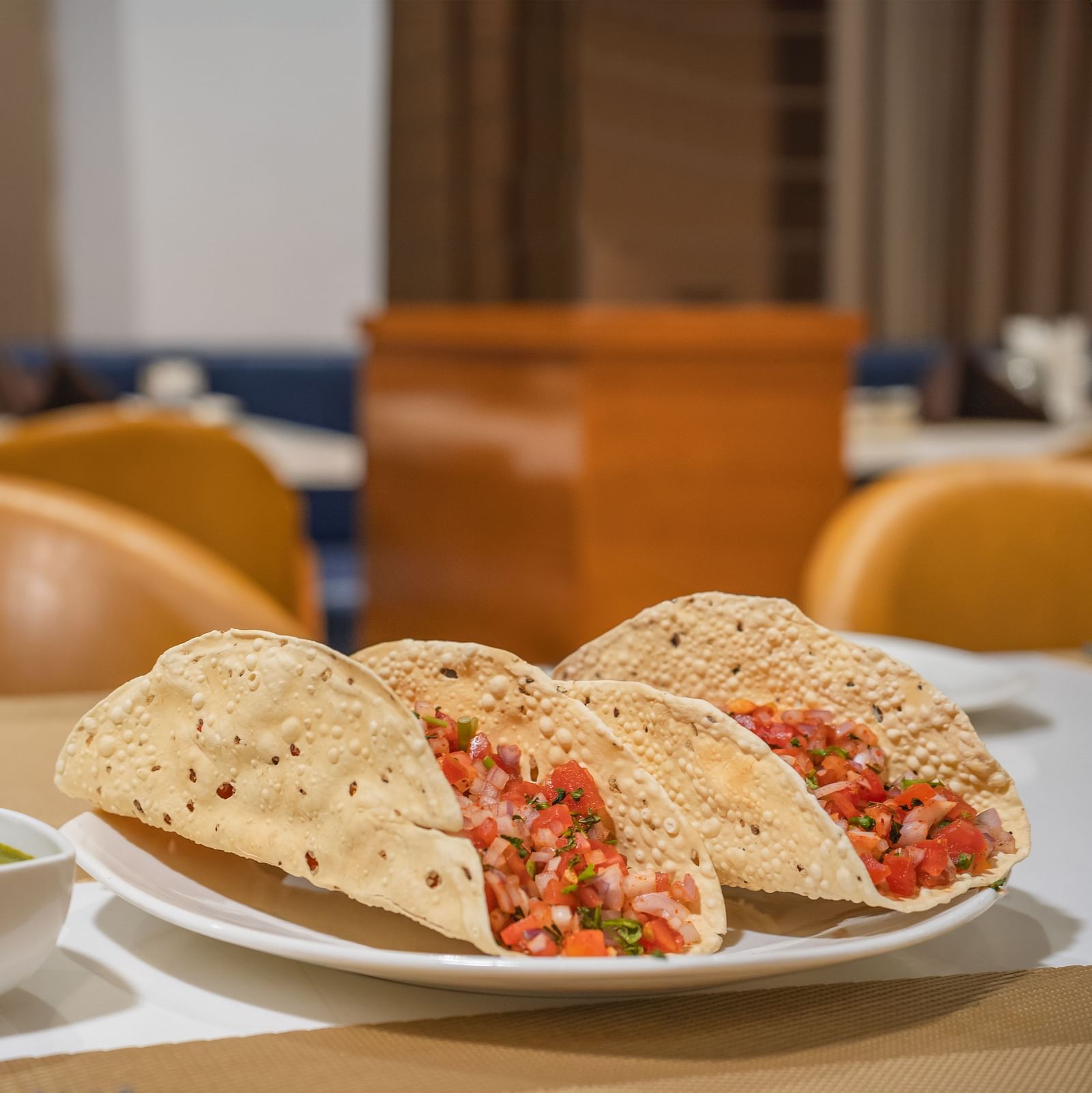 Three crispy shells filled with a vibrant mixture are served on a plate with a small bowl of green sauce