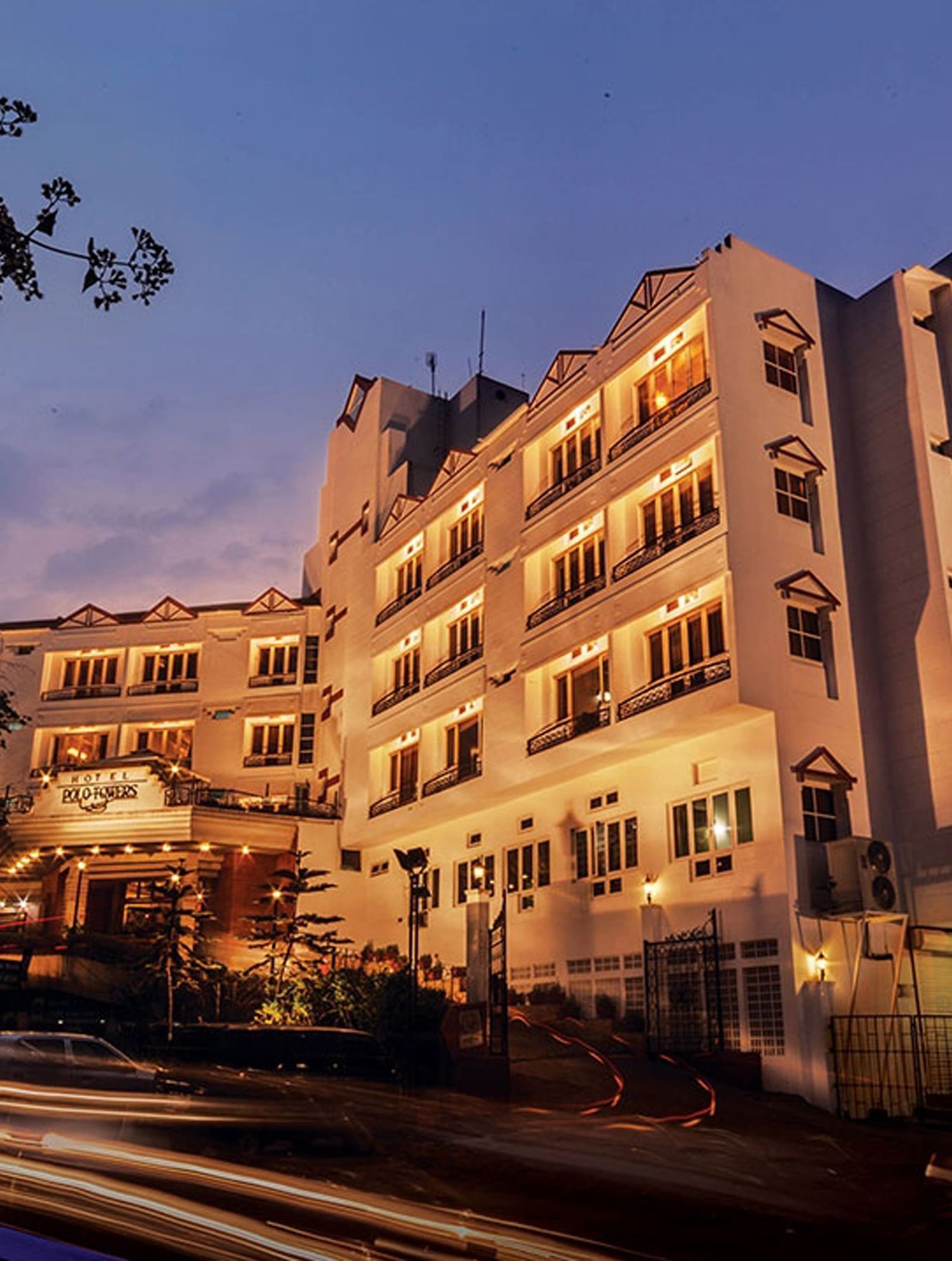 A low-angle exterior shot of the Polo Hotel Shillong, lit up in the evening with light trails from a vehicle.