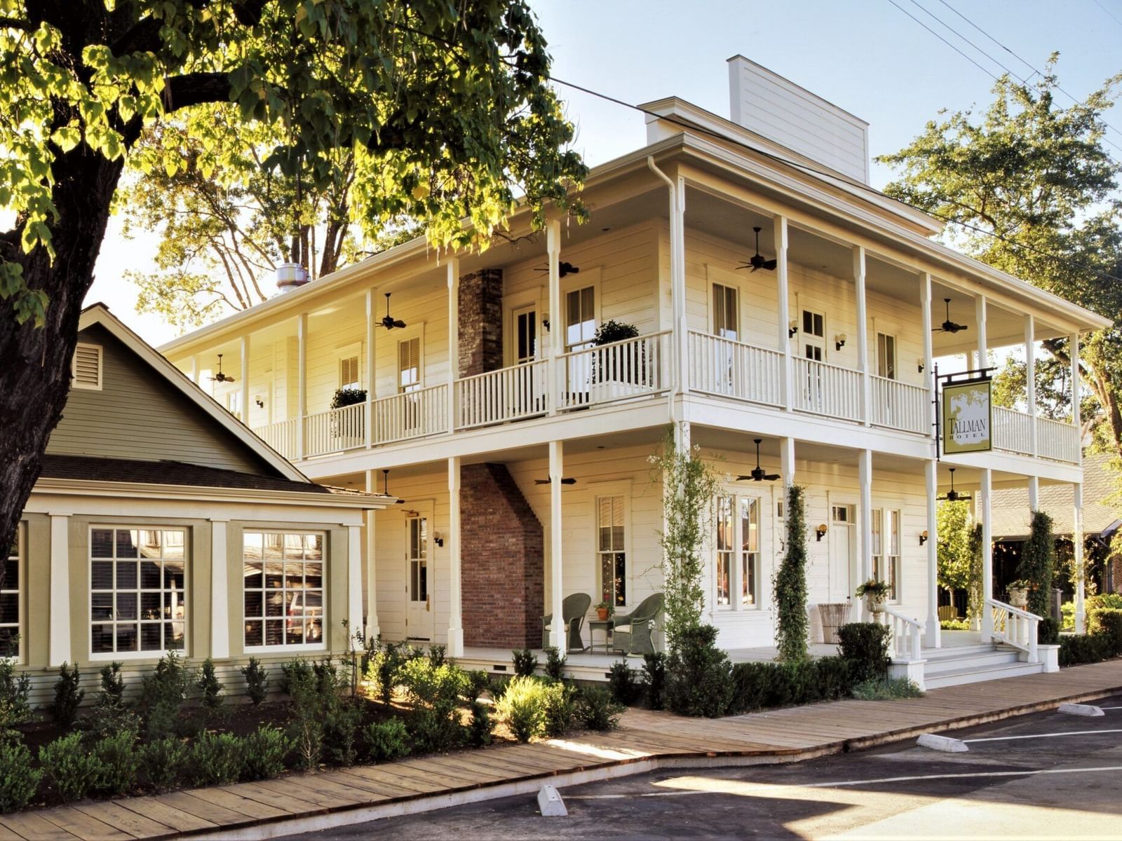 Corner view of Tallman Hotel showing two-story floor with wraparound balconies surrounded by greenery.