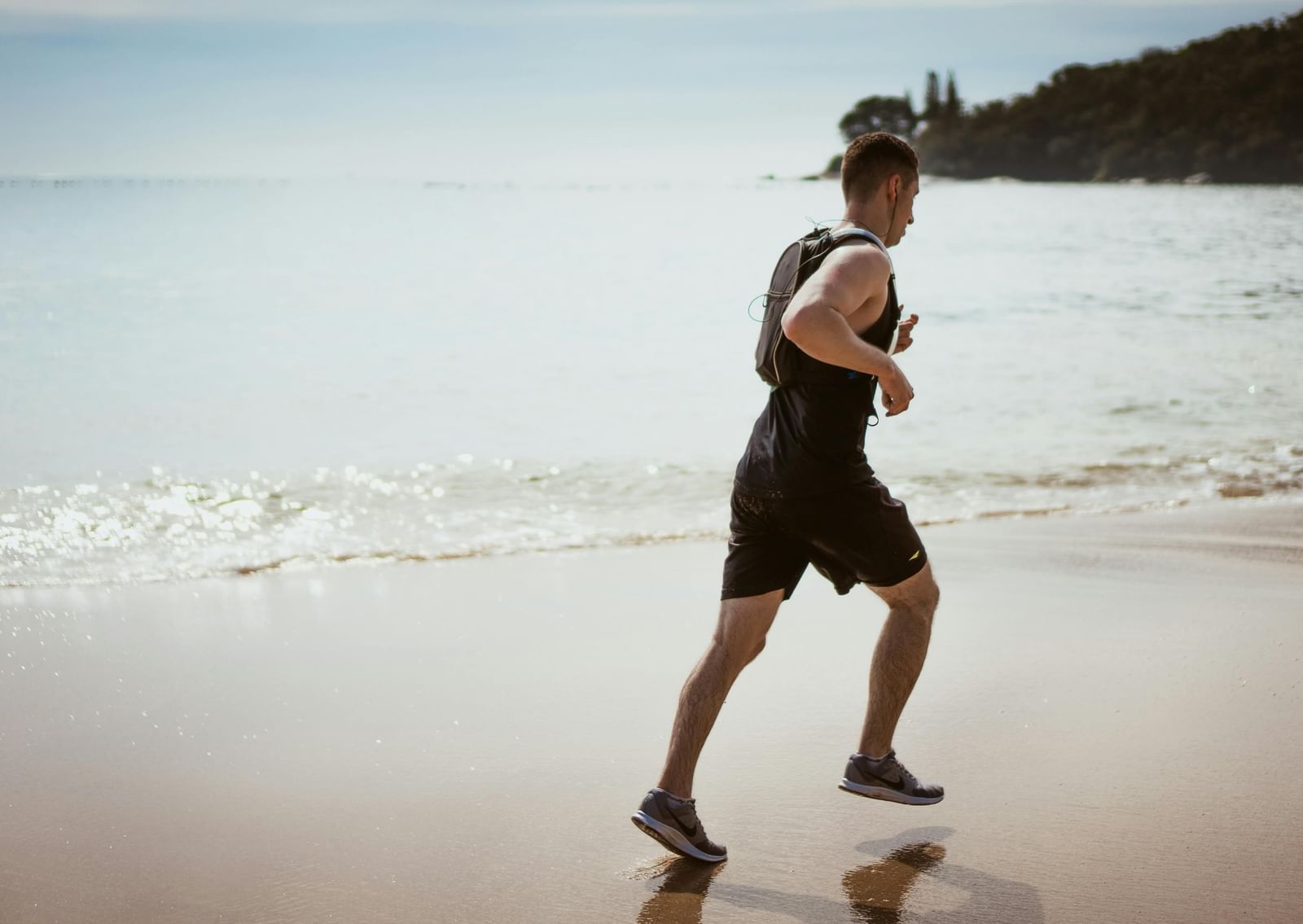 Man jogging along a quiet beach shoreline with gentle waves and a distant rocky outcrop in the background.