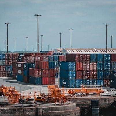A port or shipping yard filled with numerous stacked cargo containers and several tall light poles under an overcast sky.