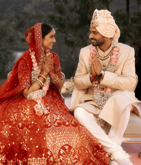 Bride and groom seated together in traditional wedding attire at Lake Gardens Lower venue with hills and trees in the background | YAAN Udaipur