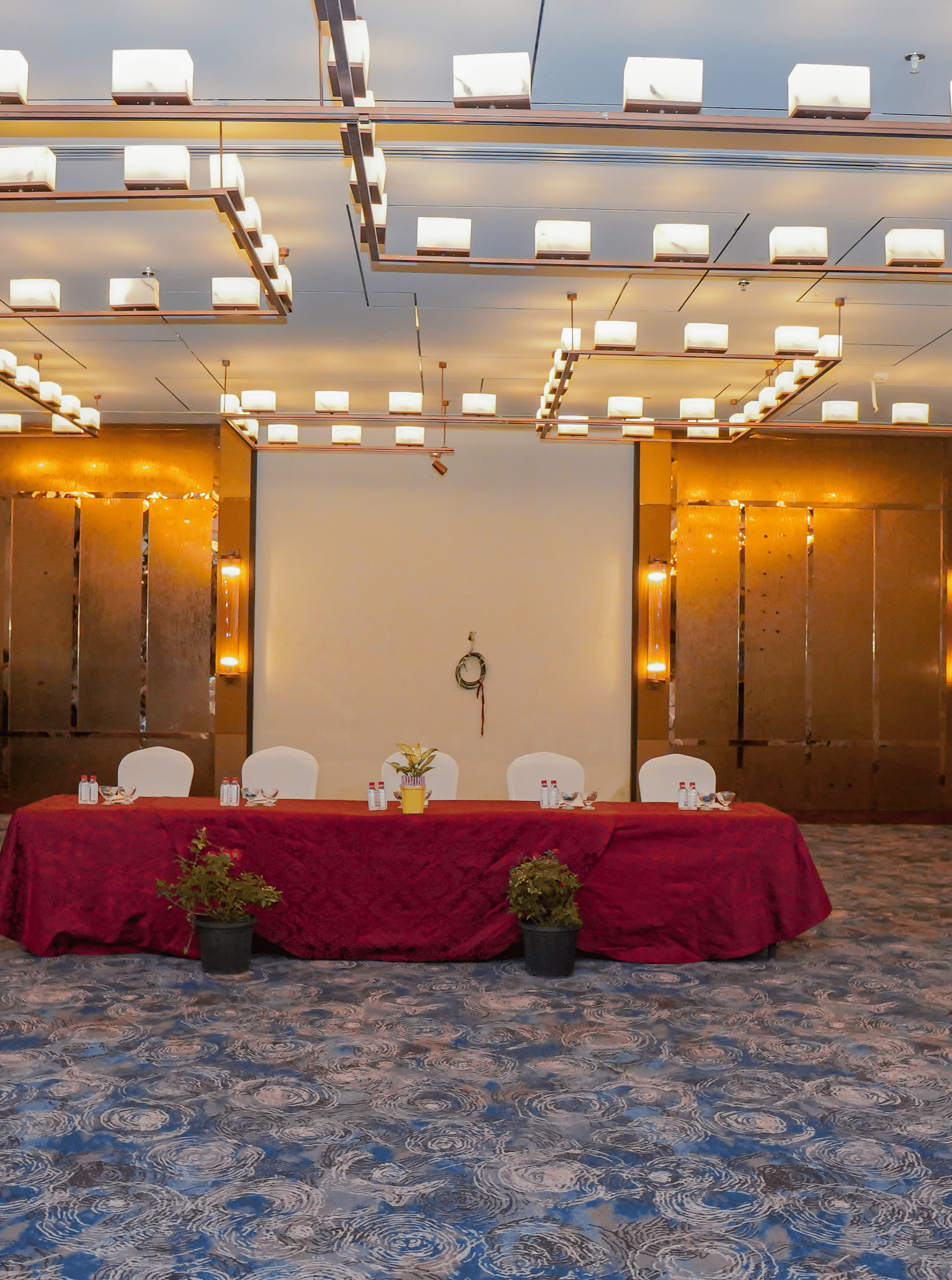 A photo of a stage area in an event room, with a table draped in a red cloth and a podium, waiting for a speaker.