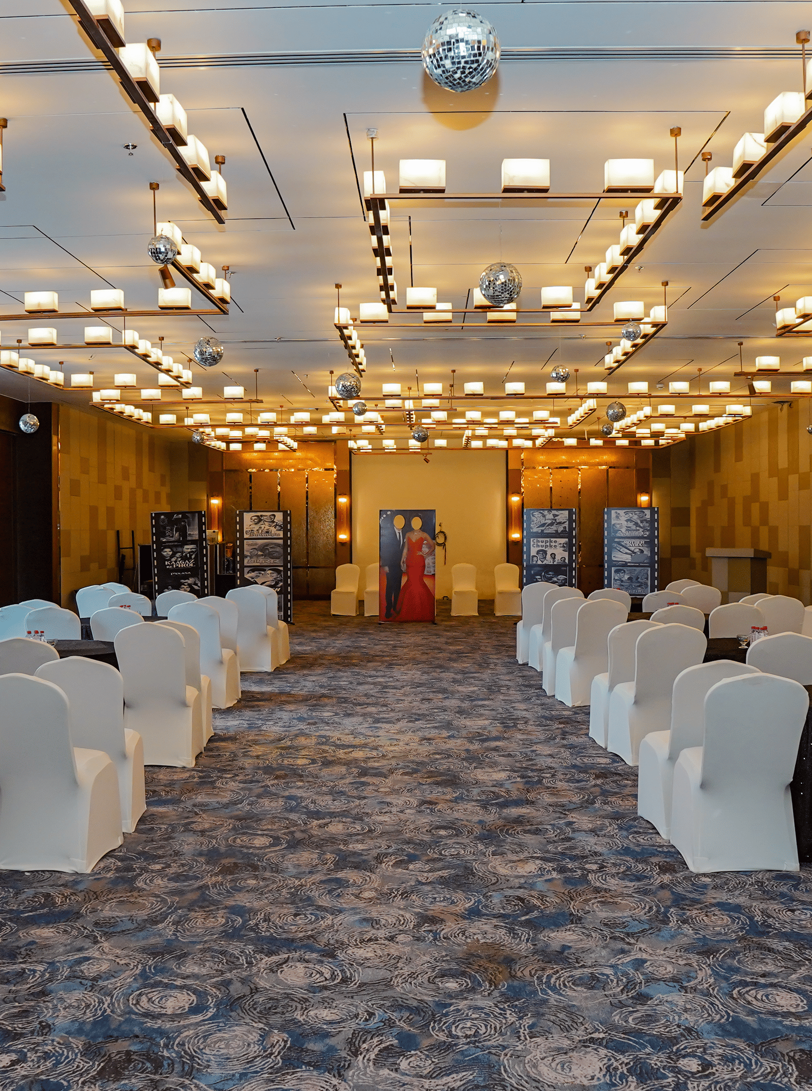 A view of a long event hall set up with multiple rows of chairs for an audience, showing the full length of the room.