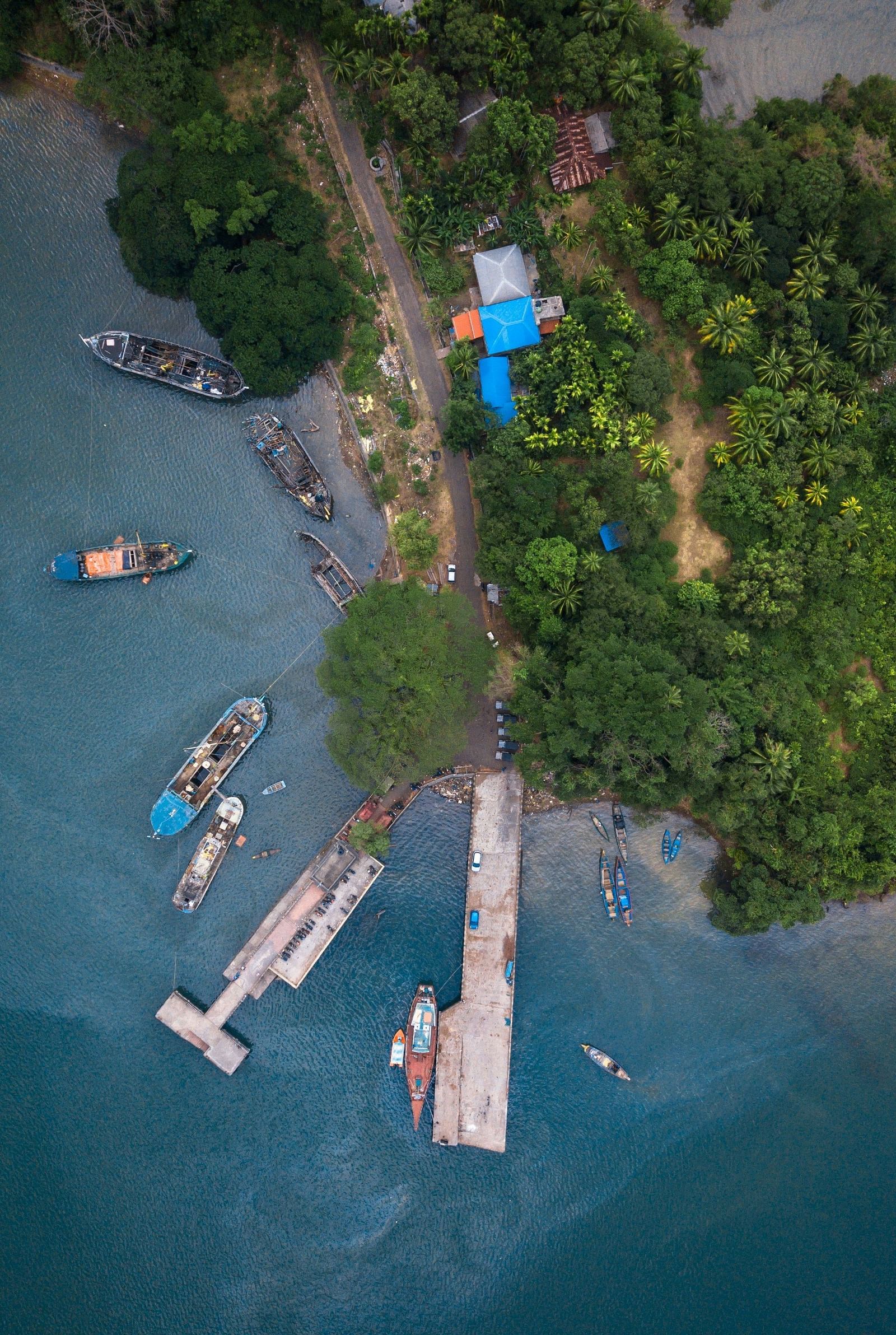 An aerial shot of a small dock on a lush shoreline with several boats anchored in calm waters