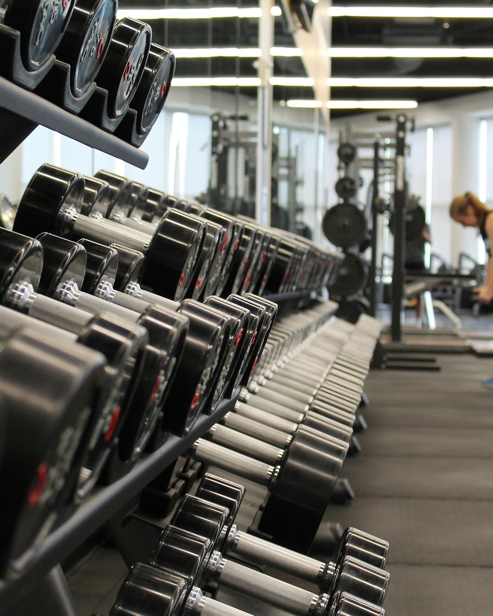 A row of dumbbells on a rack in a fitness center, with blurred figures of people exercising in the background.